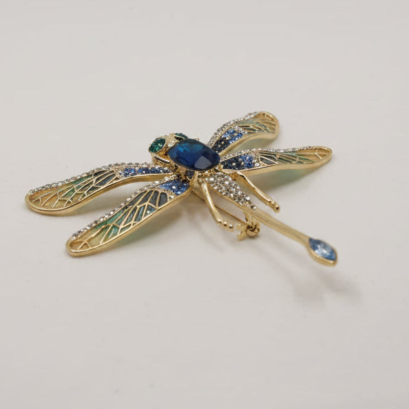 Gold dragonfly-shaped brooch with blue gemstones on a white background