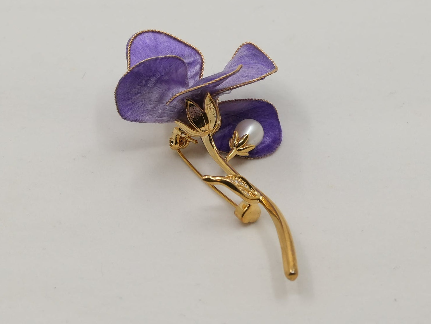 Purple flower-shaped brooch on a gold stem against a light gray background