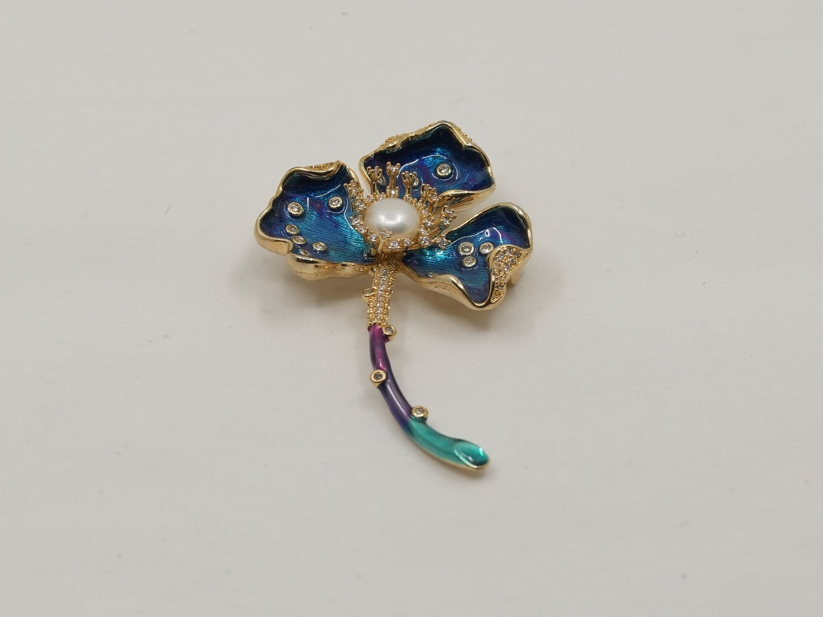 Gold four-leaf clover charm with blue stones on a light gray background