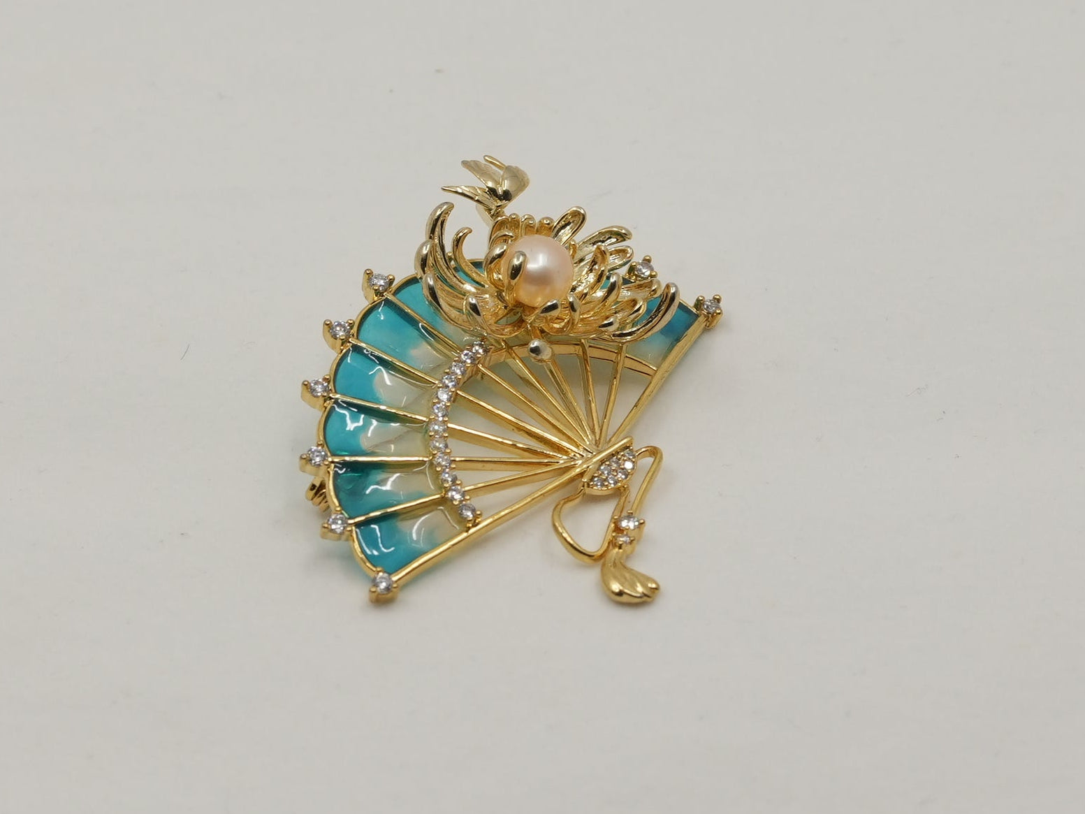 Gold brooch with turquoise stones on a light gray background