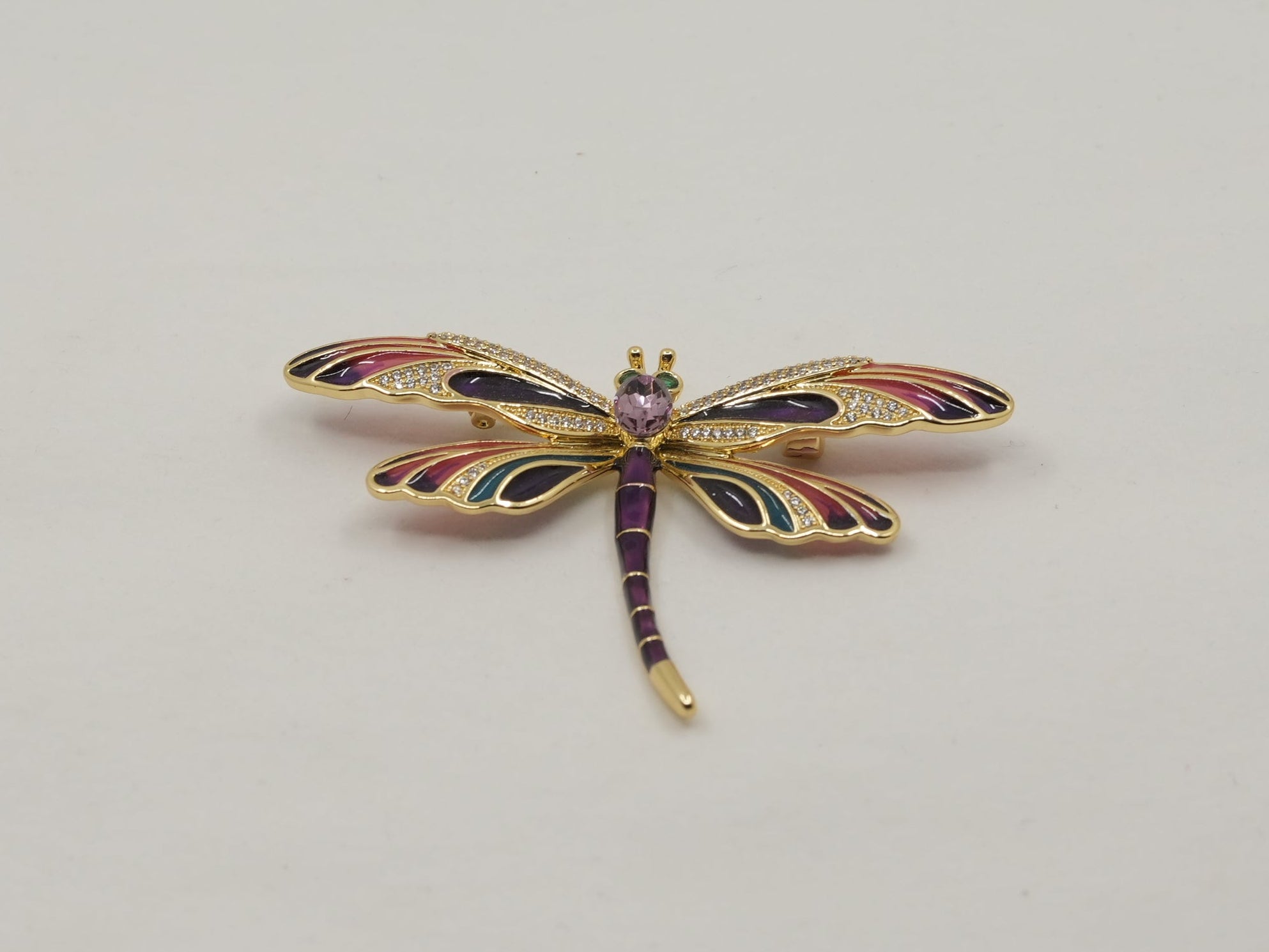 Decorative dragonfly brooch with multicolor gemstones on a light gray background