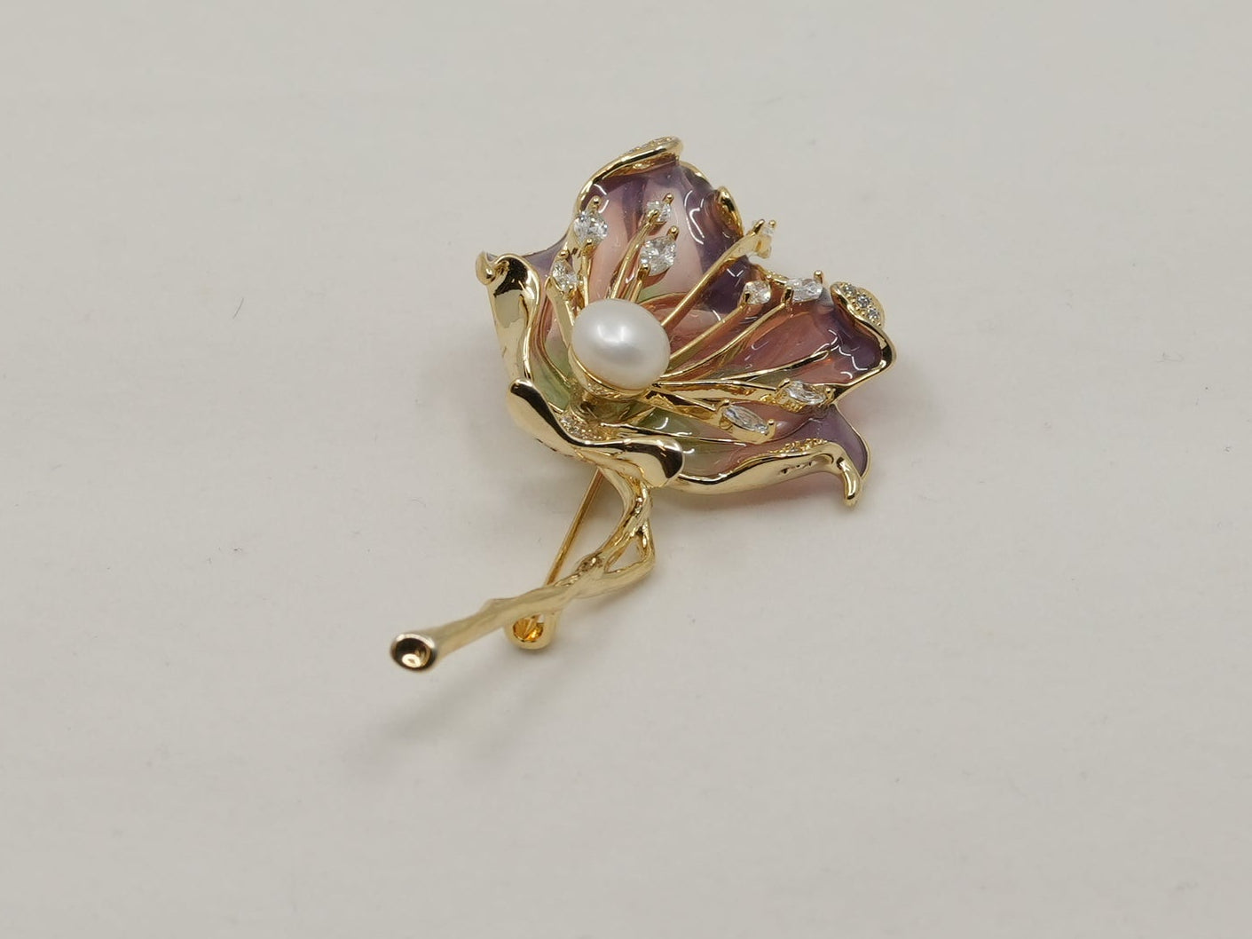 Gold brooch with a central pearl on a light gray background