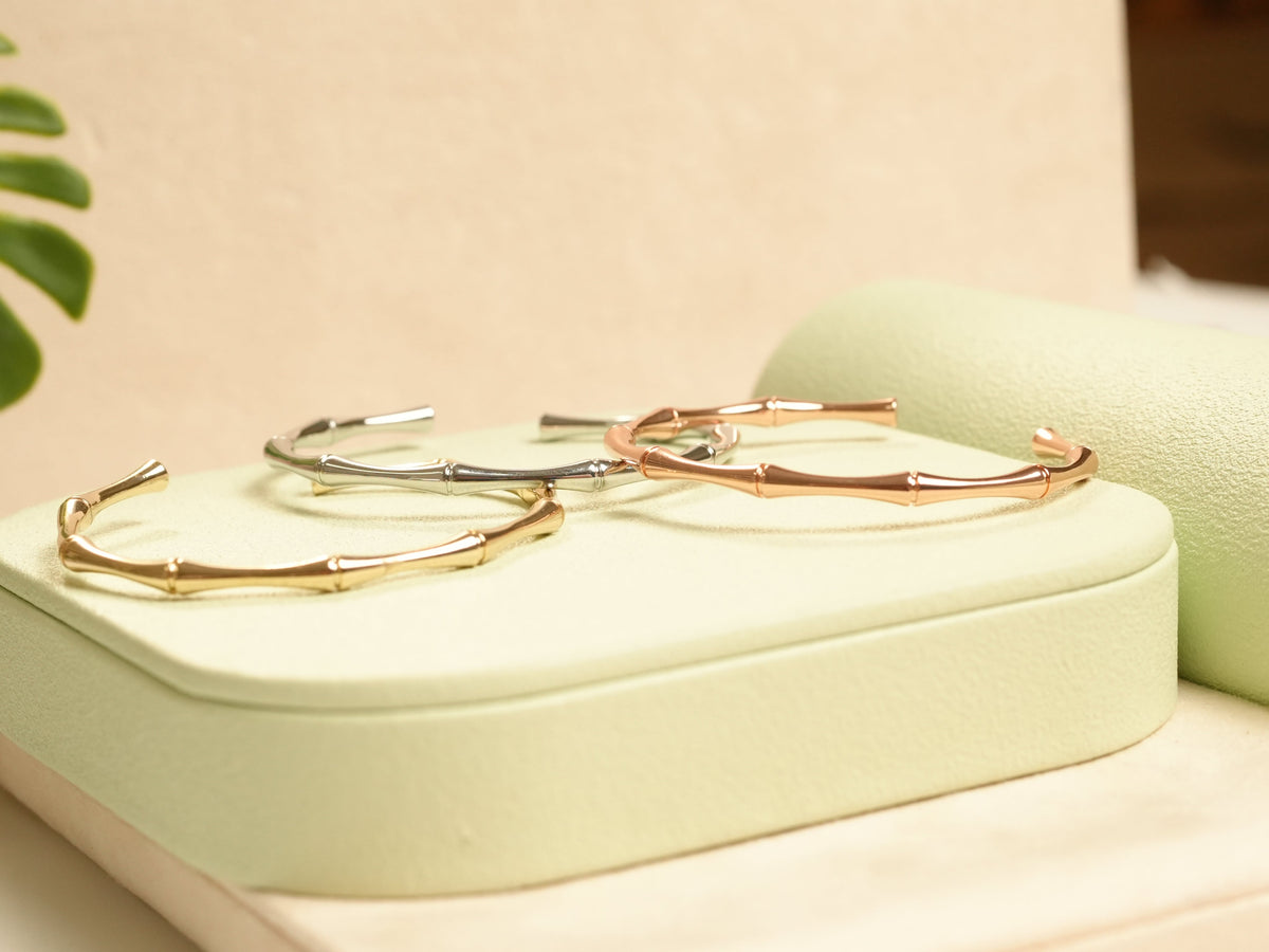 Daga-accessories bamboo-inspired bracelets in rose gold, silver, and gold tones displayed on a soft green stand.