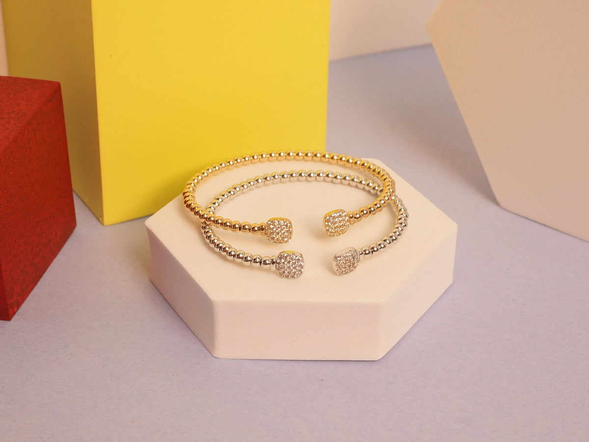 Daga-accessories beaded cuff bracelets with square-cut stone accents in gold and silver tones on a geometric stand.