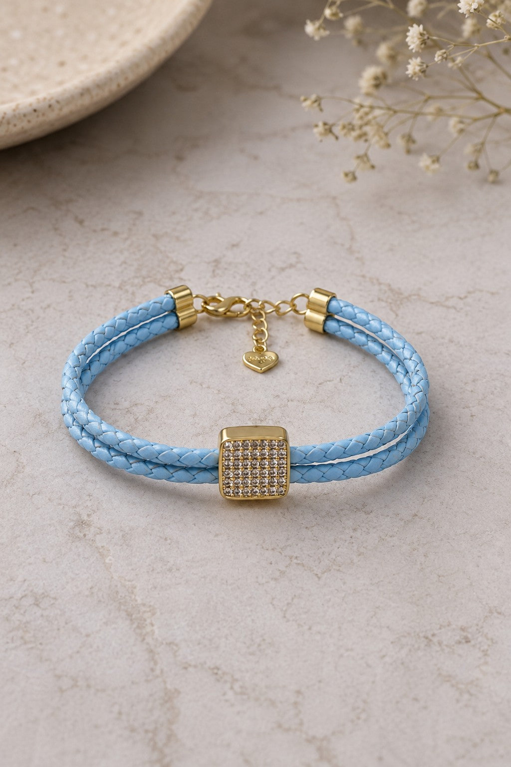Daga-accessories light blue braided leather bracelet with a gold-toned square crystal ornament and heart charm.