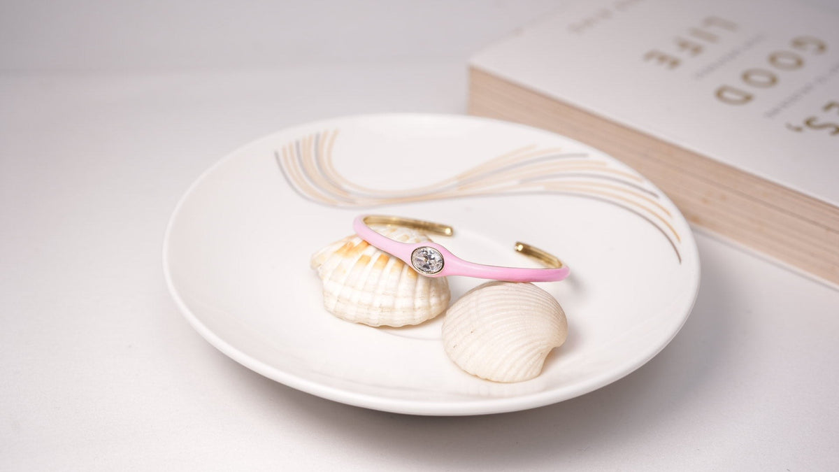 Daga-accessories blush crystal cuff bracelet with a single central stone resting on seashells in a ceramic dish