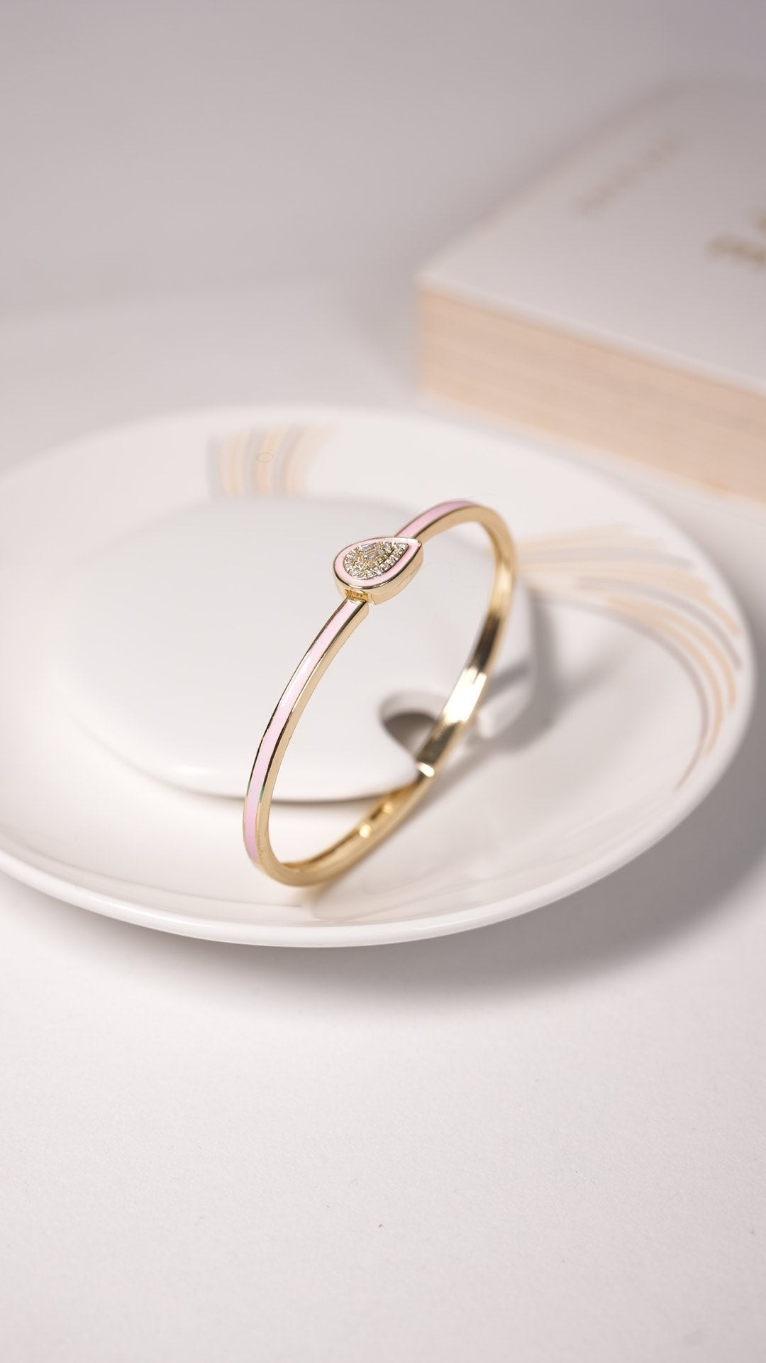Daga-accessories blush shine drop bracelet featuring a gold band with a delicate teardrop charm on a white plate.
