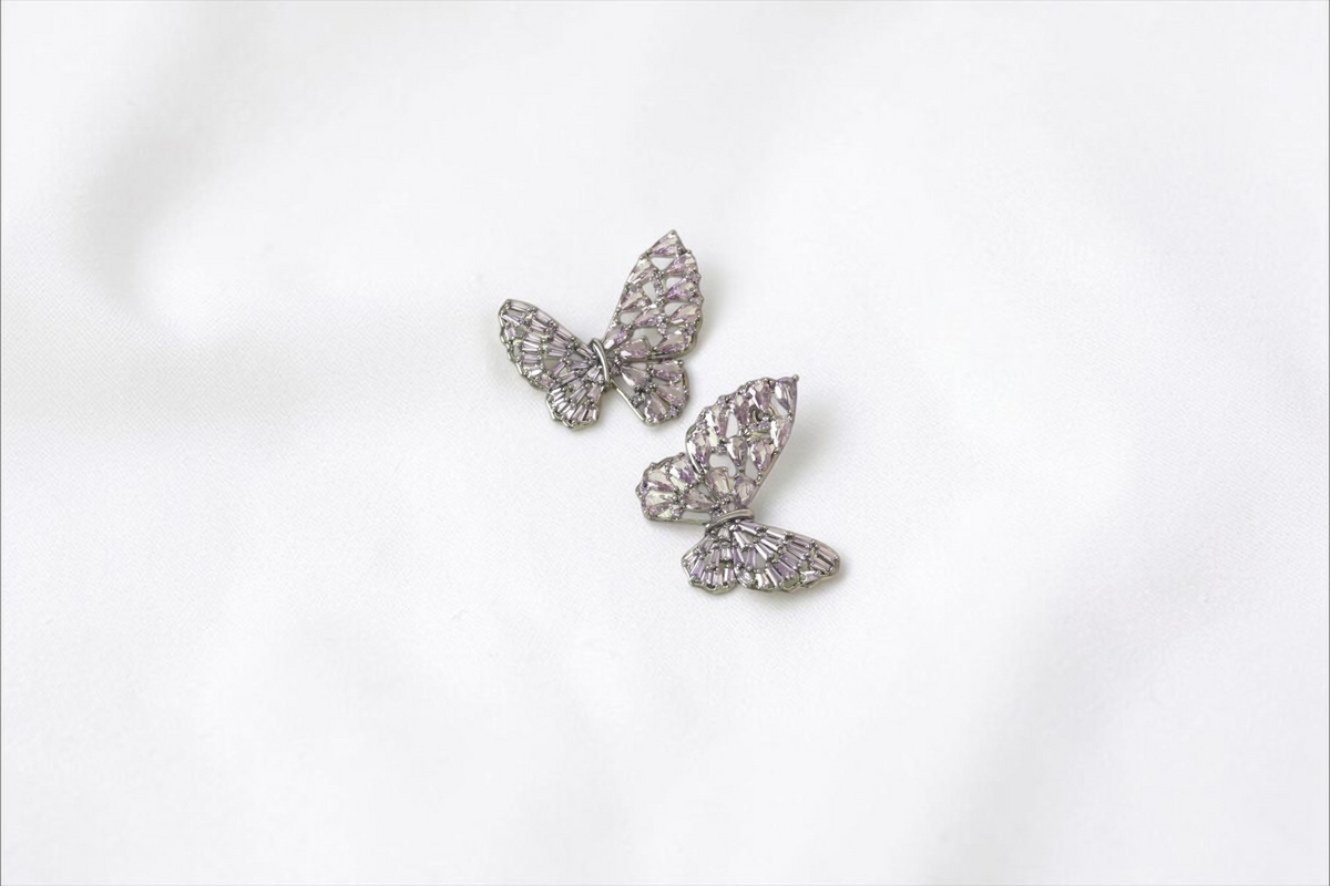 Daga-accessories butterfly stud earrings with lavender crystals set in a gunmetal frame on a light green display pad.