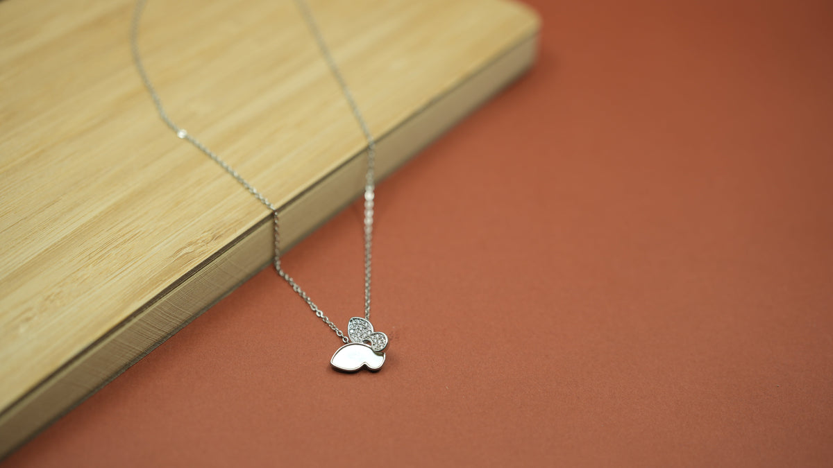 Daga-accessories silver butterfly pendant necklace with pavé stones and smooth inlay on a wooden surface