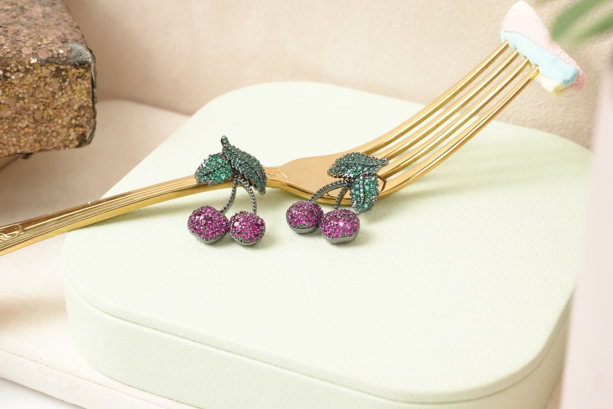 Daga-accessories cherry stud earrings with pink and green crystal stones set in a dark gunmetal finish on a gold fork.