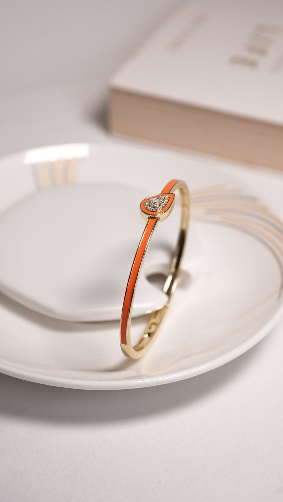 Daga-accessories gold-tone bangle bracelet with a vibrant coral enamel inlay and a sparkling teardrop charm.
