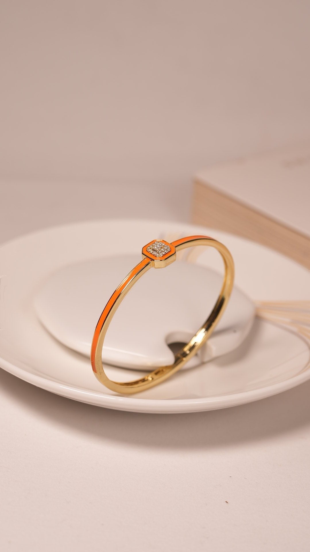 Daga-accessories coral emblem bracelet in gold with a vibrant orange enamel inlay and a sparkling square centerpiece.