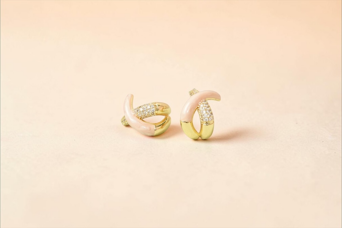 Daga-accessories gold-toned crisscross hoop earrings with pastel pink enamel and cubic zirconia accents on a display
