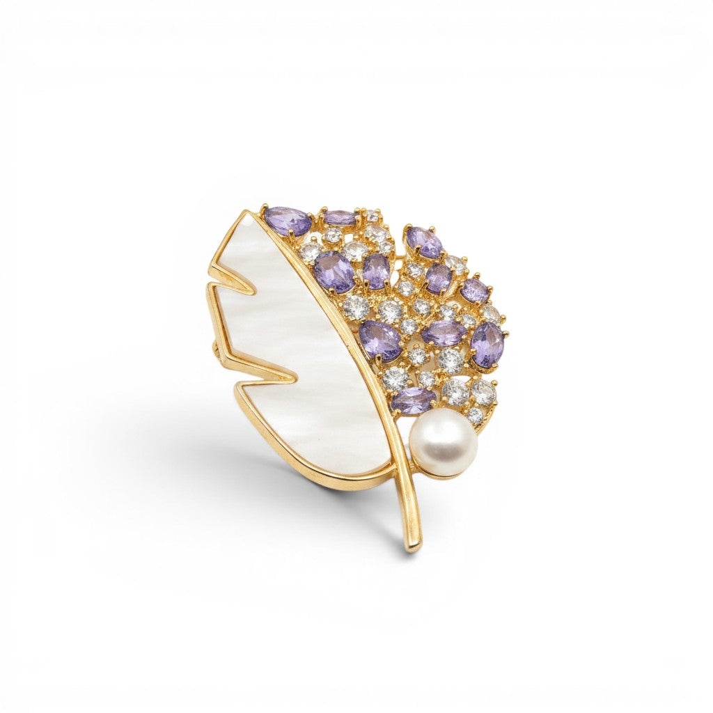 Daga-accessories gold-tone leaf brooch featuring purple crystals, clear stones, and a lustrous white pearl accent.