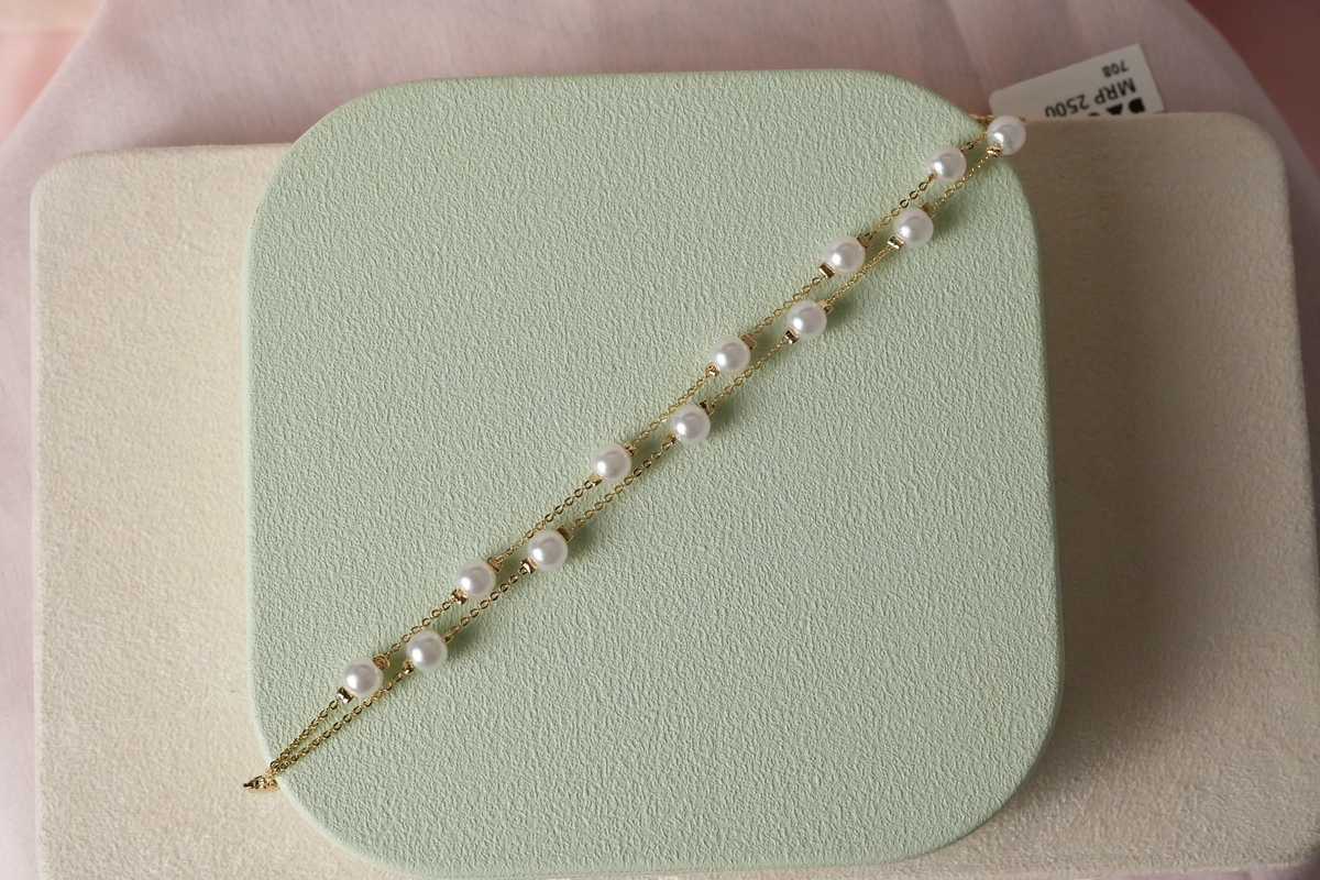 Daga-accessories double layer bracelet with white pearls on a delicate gold-toned chain displayed on a green stand.