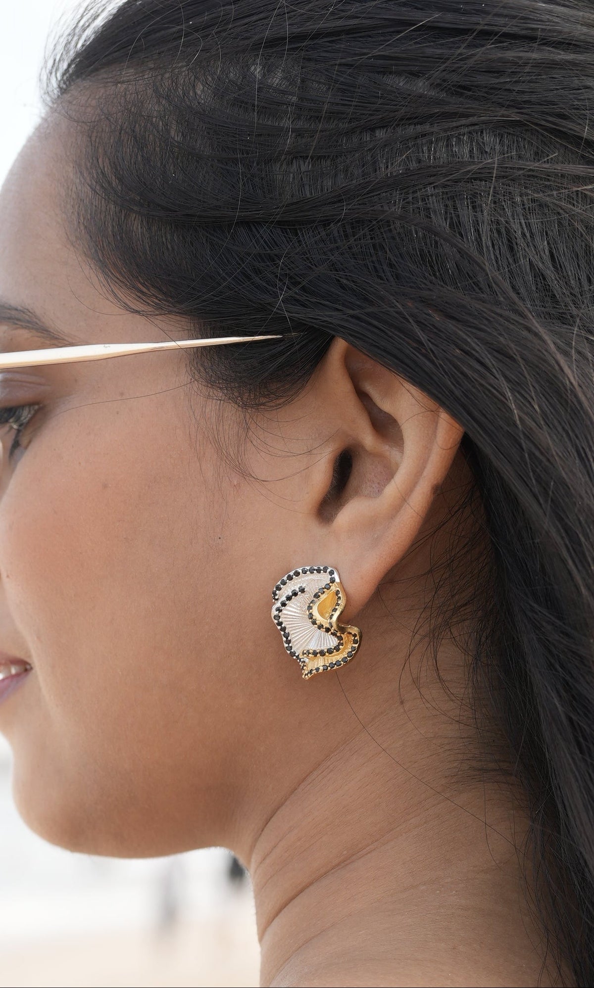 Daga-accessories Dual Tone Elegance Stud earring featuring gold, silver, and black stones worn on a woman's ear