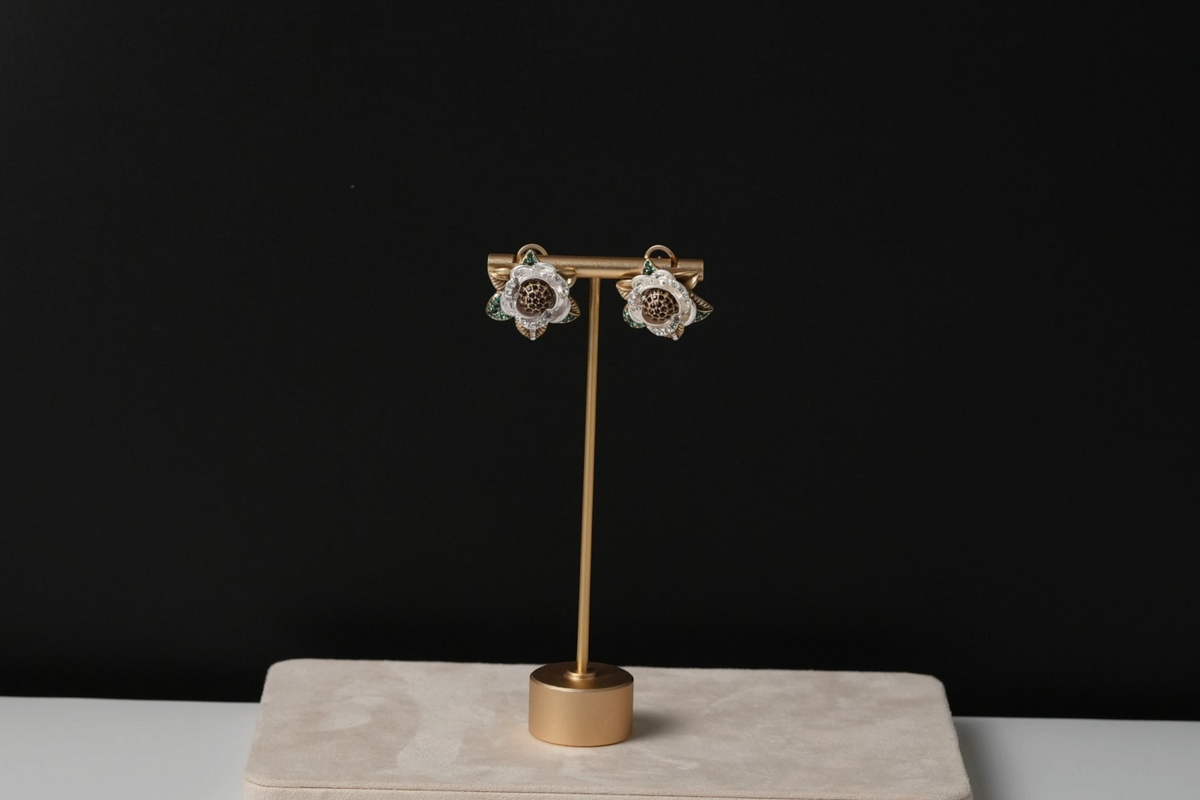 Daga-accessories floral earrings with gold tone, white petals, and green leaf accents on a display stand.
