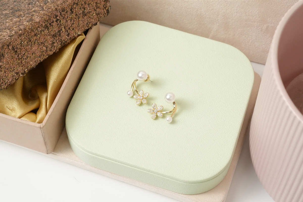 Daga-accessories floral stud earrings with cubic zirconia, gold-toned frames, and faux pearls on a light green stand.