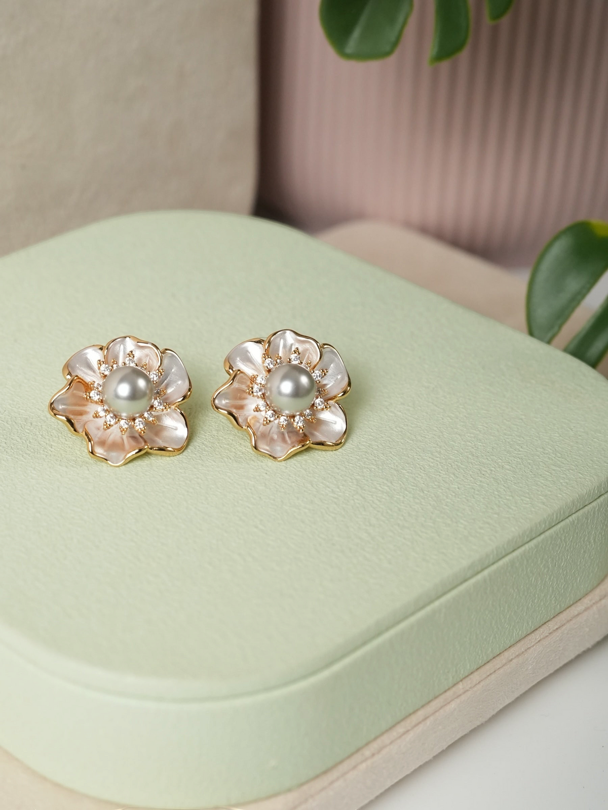 Daga-accessories floral stud earrings with iridescent petals, central pearl, and gold-tone setting on green display.