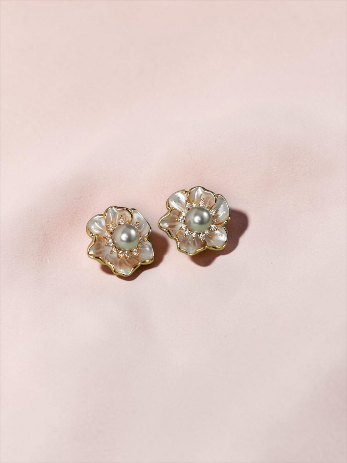 Daga-accessories floral stud earrings with iridescent petals, central pearls, and gold-tone settings on a green base.