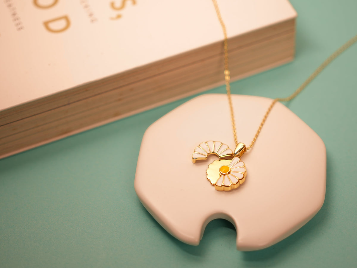 Daga-accessories Floral Whisper Necklace featuring a gold chain and a delicate white and yellow enamel flower pendant.