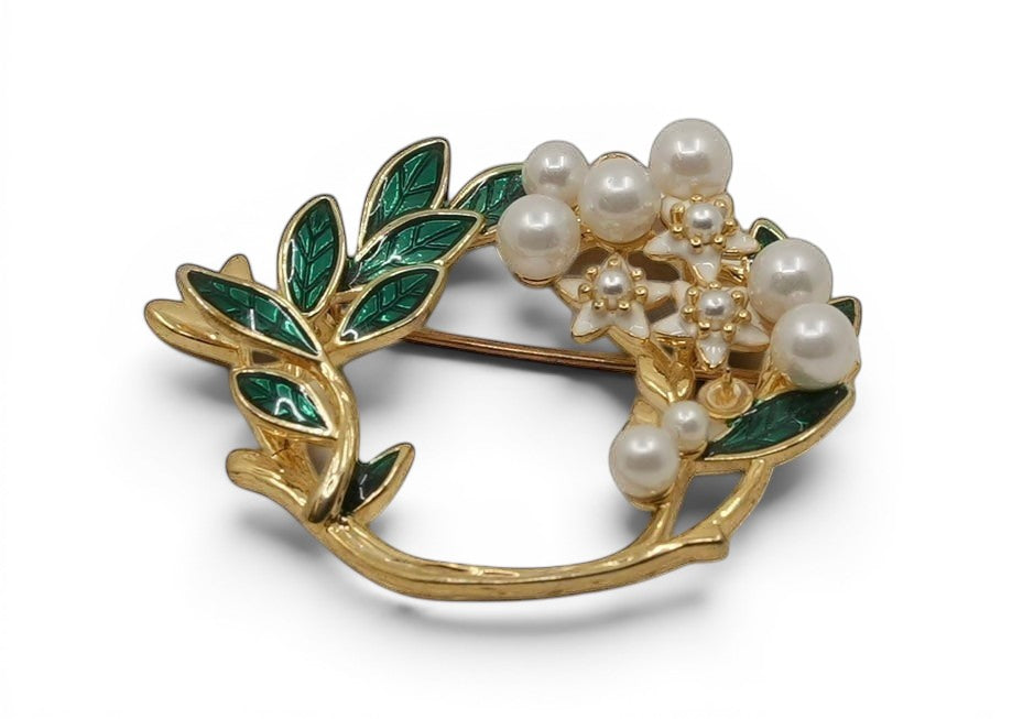 Daga-accessories floral wreath brooch with green enamel leaves, white flowers, and faux pearls in gold-tone metal.