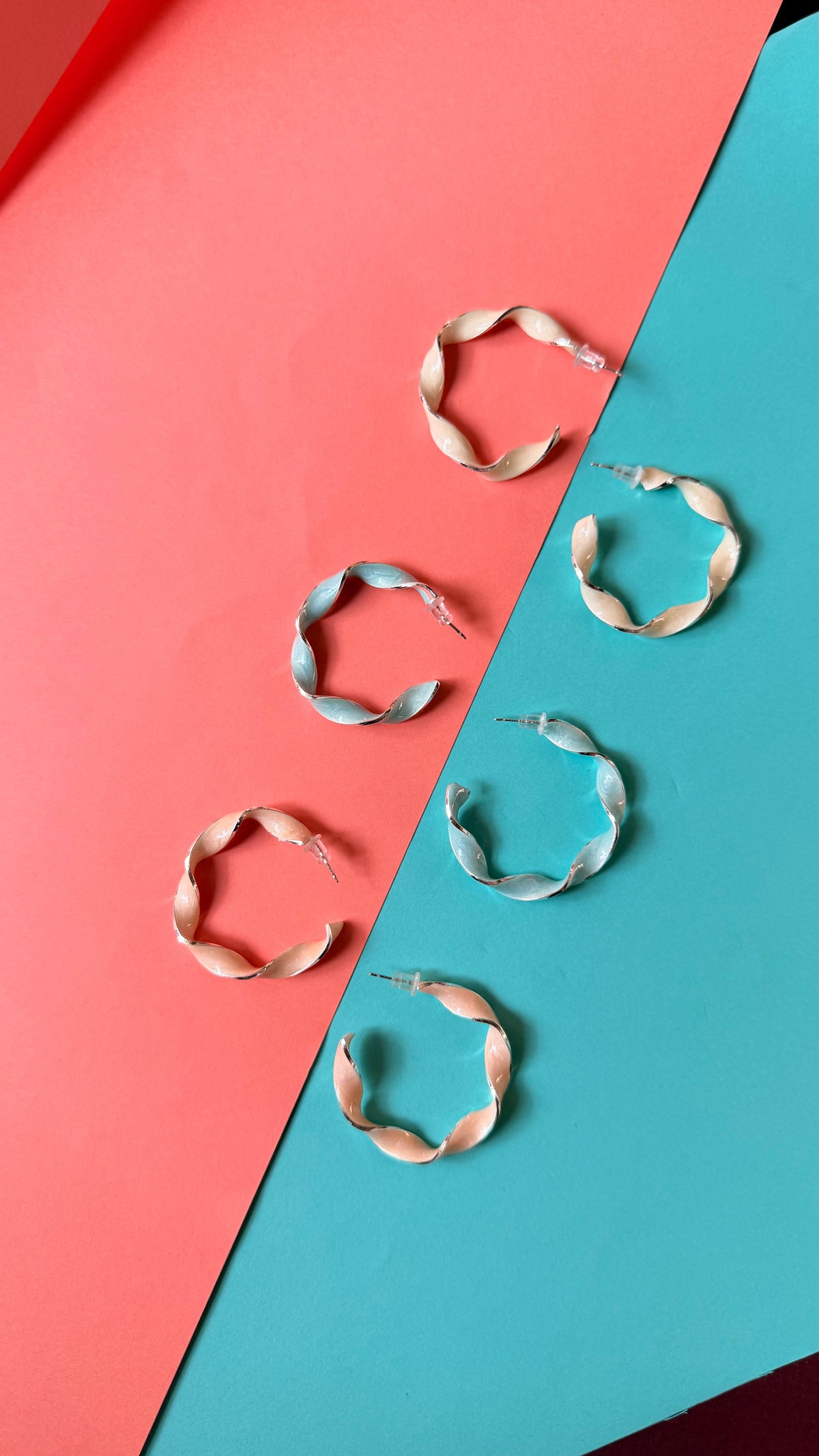 Daga-accessories Serene Fusilli hoop earrings in pastel spiral designs arranged on a coral and teal background