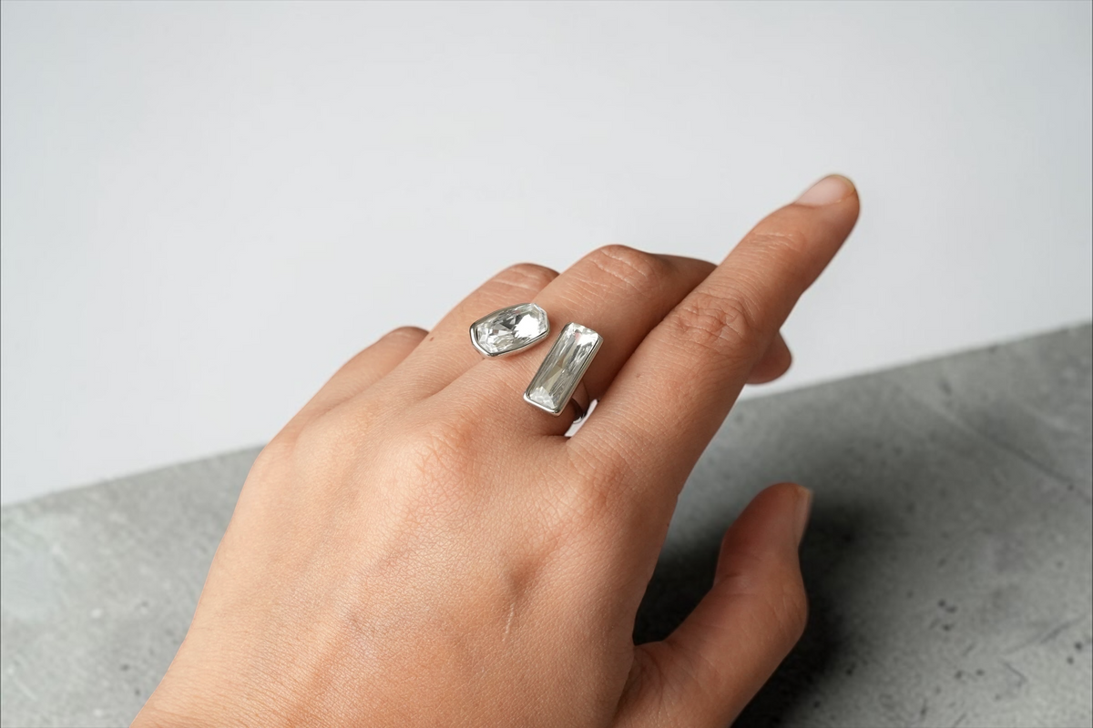 Daga-accessories silver-tone open ring with a baguette and cushion cut crystal on a hand against a dark background.
