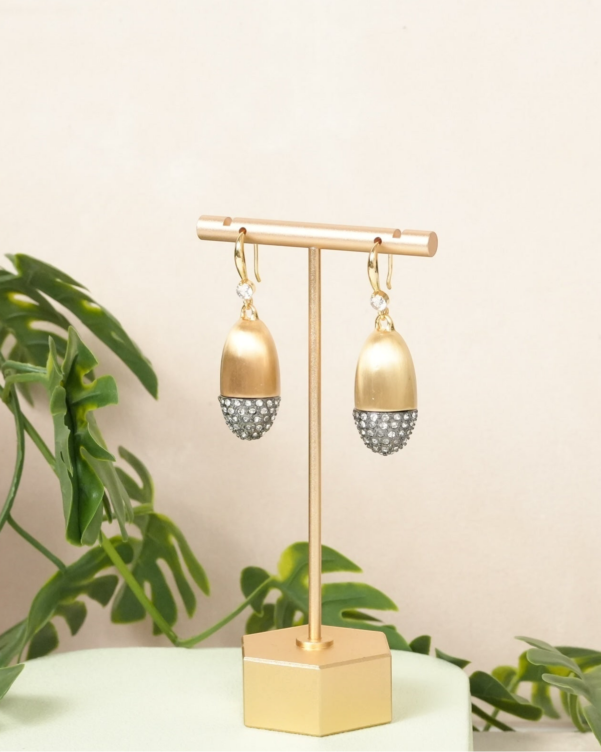 Daga-accessories gold-toned acorn-shaped drop earrings with crystal-encrusted bases on a display stand.