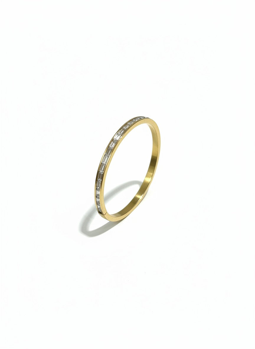 Daga-accessories gold-toned bangle bracelet featuring a row of shimmering baguette stones on a polished metal band.