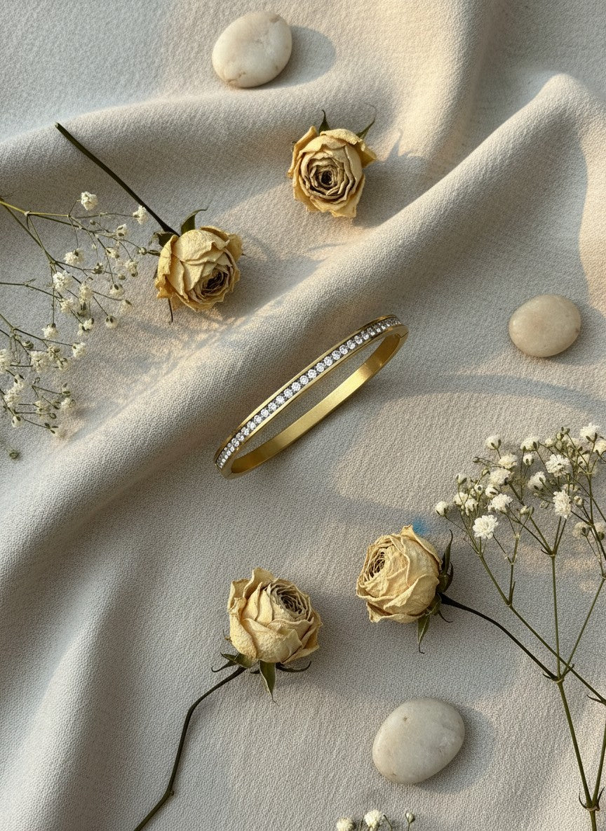 Daga-accessories gold-toned bangle bracelet with a row of cubic zirconia stones on a draped fabric background.