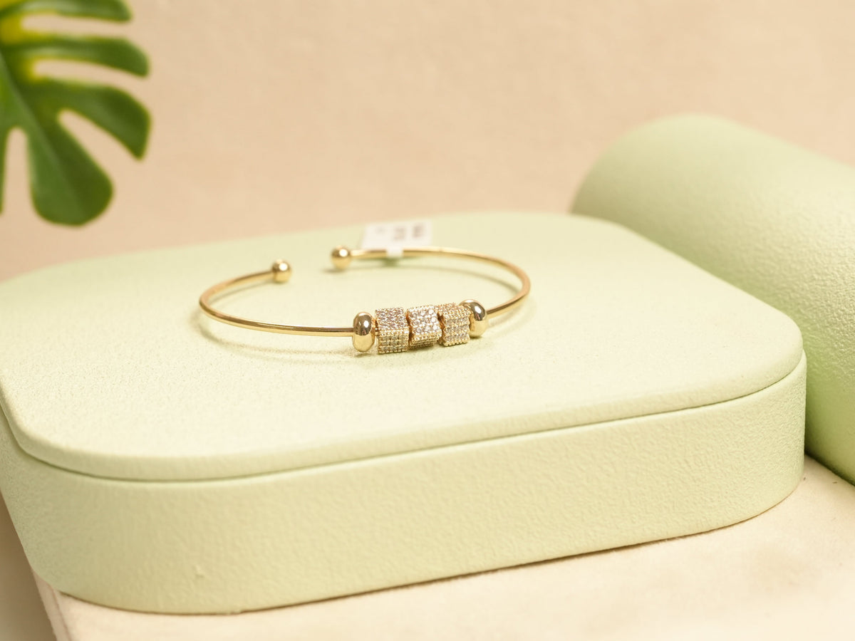 Daga-accessories gold bead bracelet featuring three pavé-set crystal cylinder charms on a sleek open cuff design.
