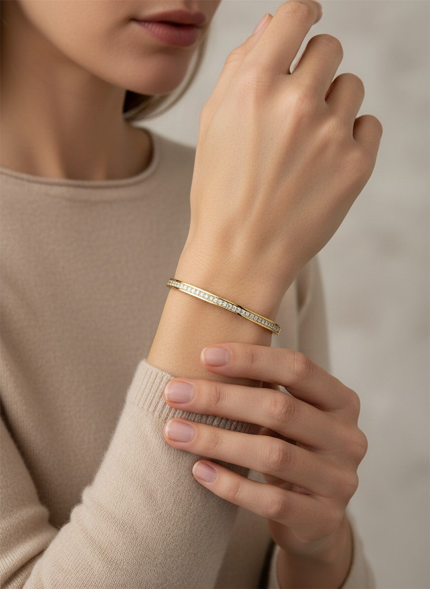 Daga-accessories gold-toned metal bangle bracelet featuring a row of clear crystals worn on a woman's wrist.