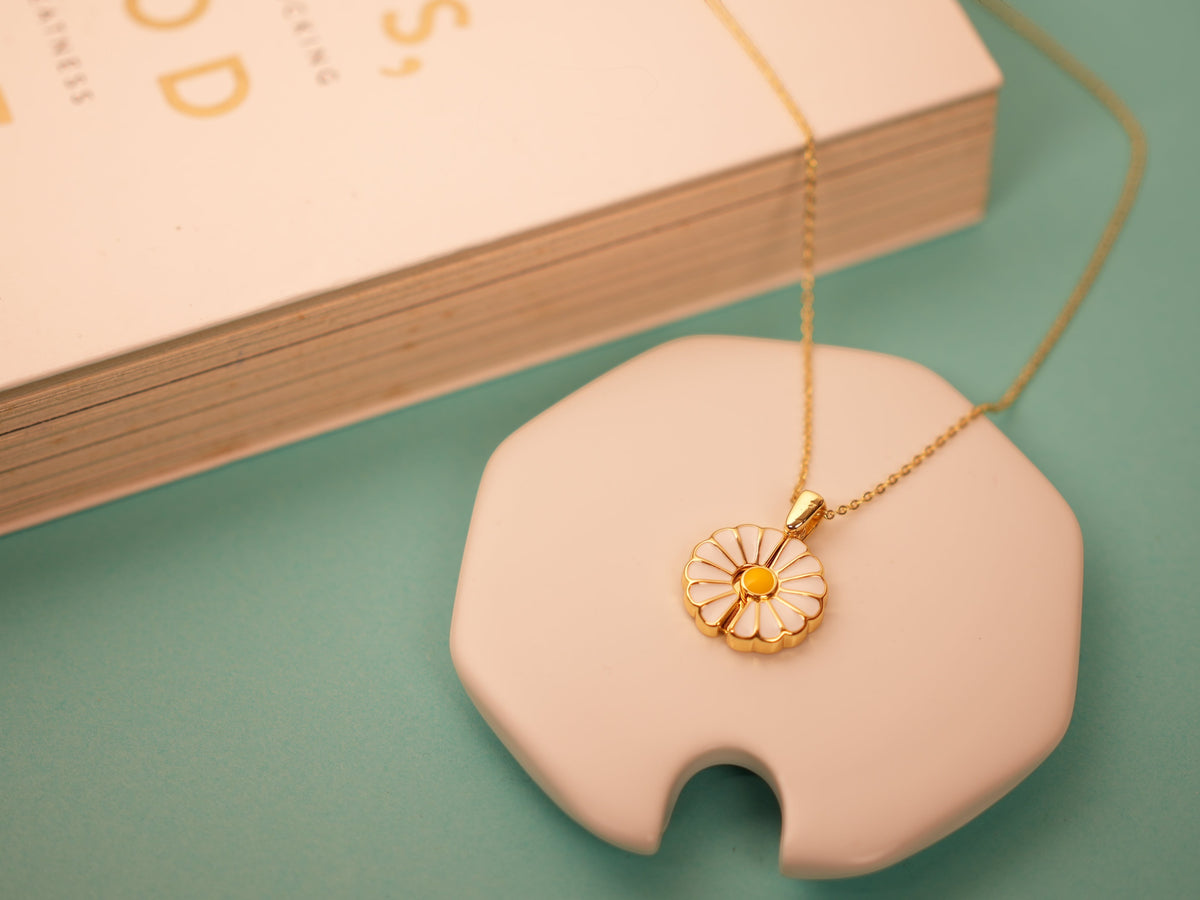 Daga-accessories Floral Whisper Necklace featuring a gold daisy pendant with white enamel petals on a delicate chain.