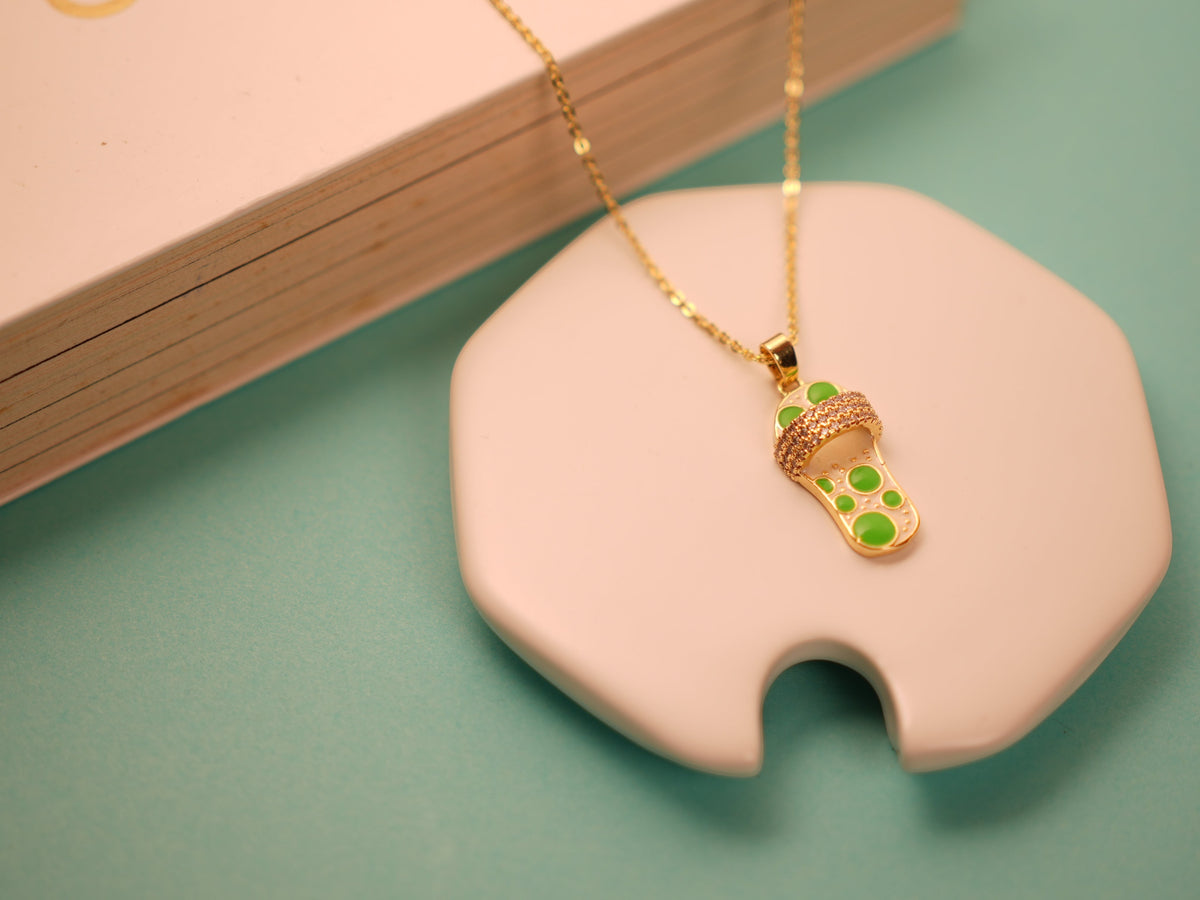 Daga-accessories gold flip-flop pendant necklace with mint green enamel accents and sparkling crystal strap detail.