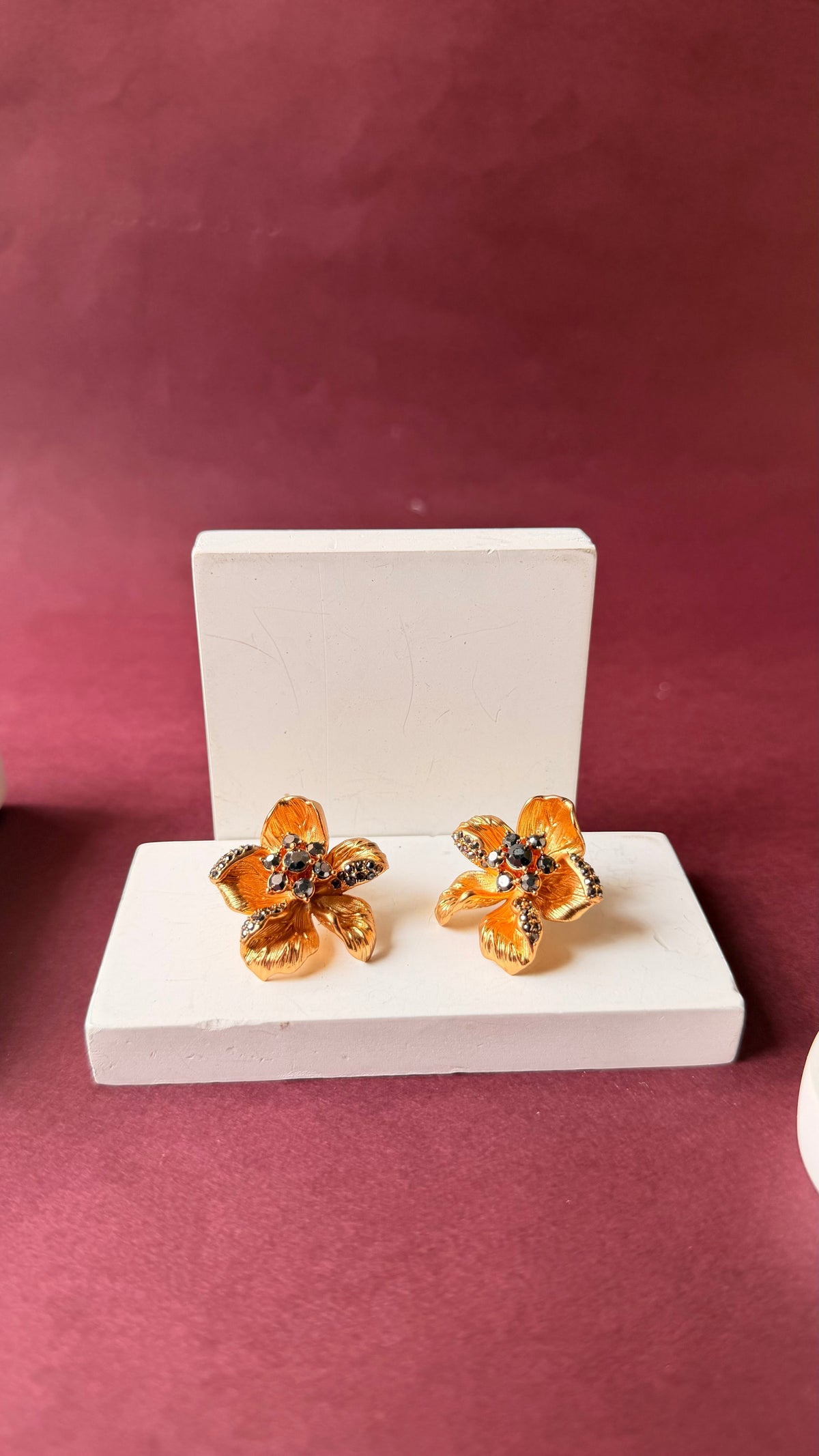 Daga-accessories Garden Glow floral earrings in gold with multicolored stone accents on a white display stand.