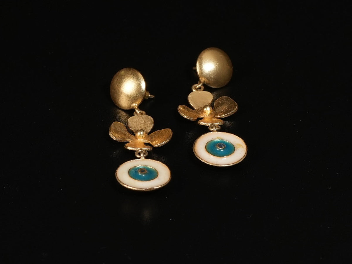 Daga-accessories gold floral drop earrings featuring a blue and white enamel evil eye charm on a black background.