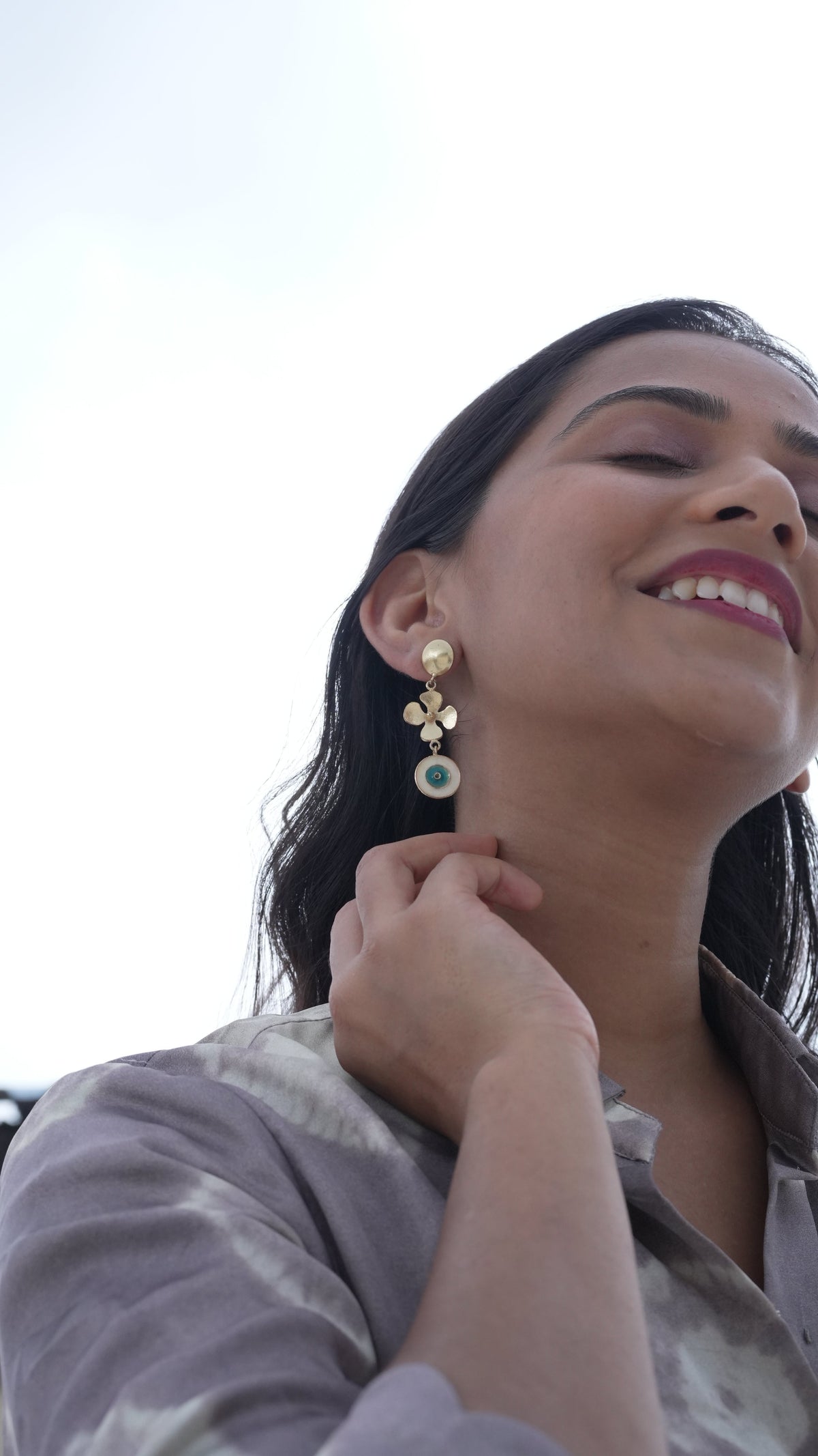 Daga-accessories gold floral earrings featuring an evil eye charm worn by a smiling woman