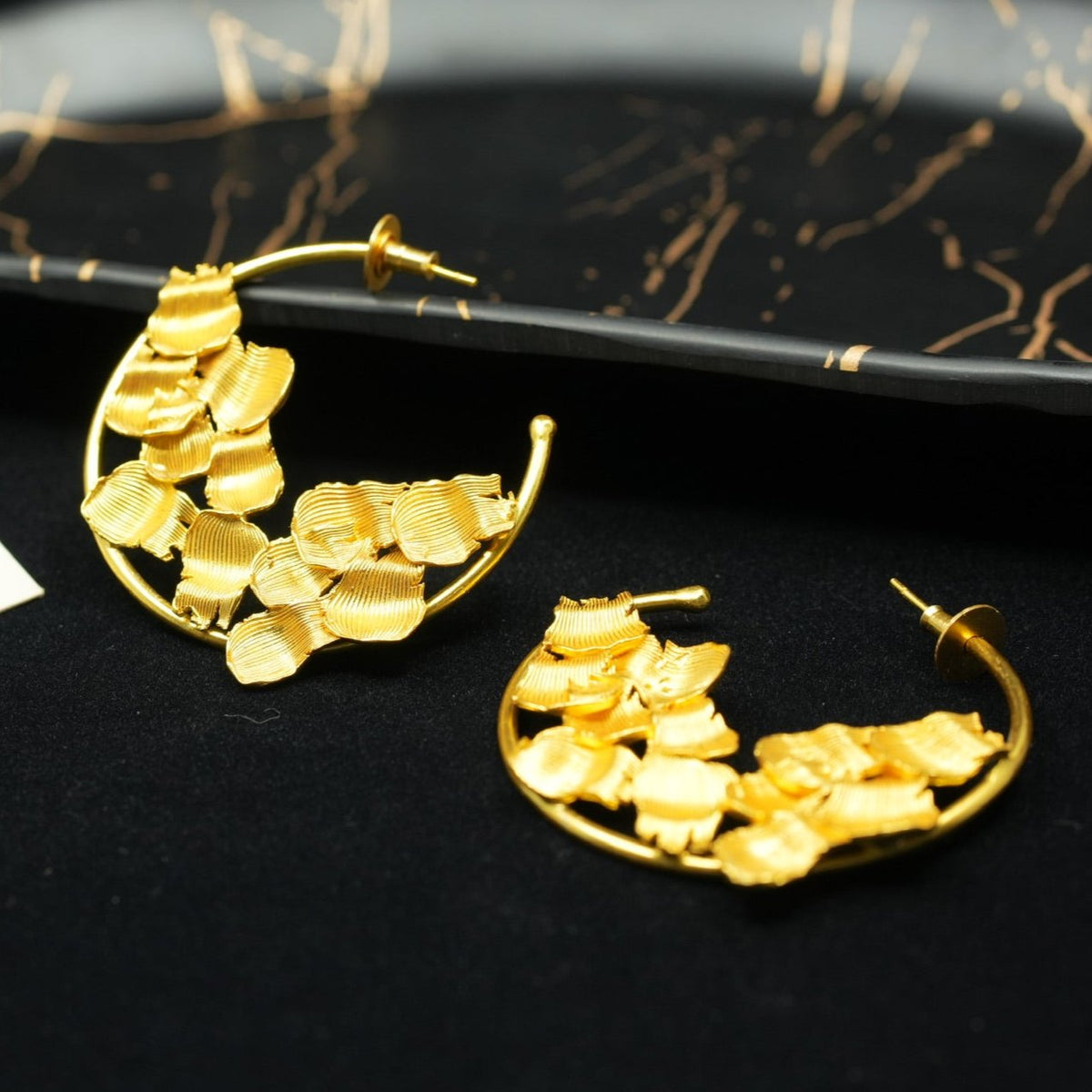 Daga-accessories gold hoop earrings featuring a sculpted floral petal design on a black display tray.