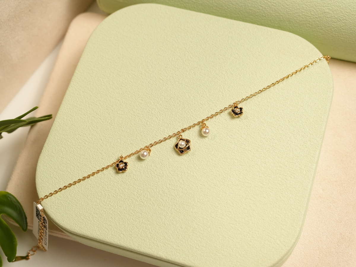 Daga-accessories gold charm bracelet featuring black enamel flowers, crystal centers, and cream faux pearls.