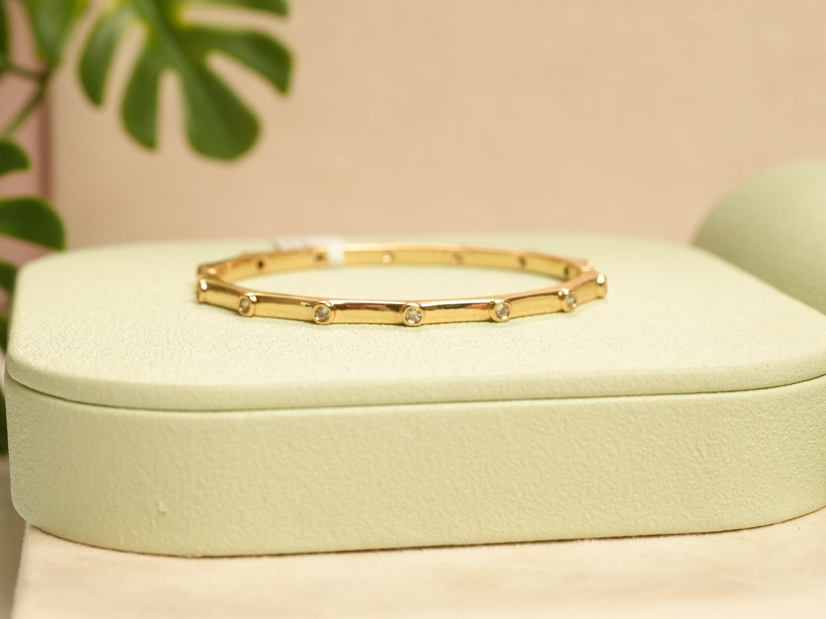 Daga-accessories gold hexagon bracelet featuring embedded diamond studs on a light green display stand