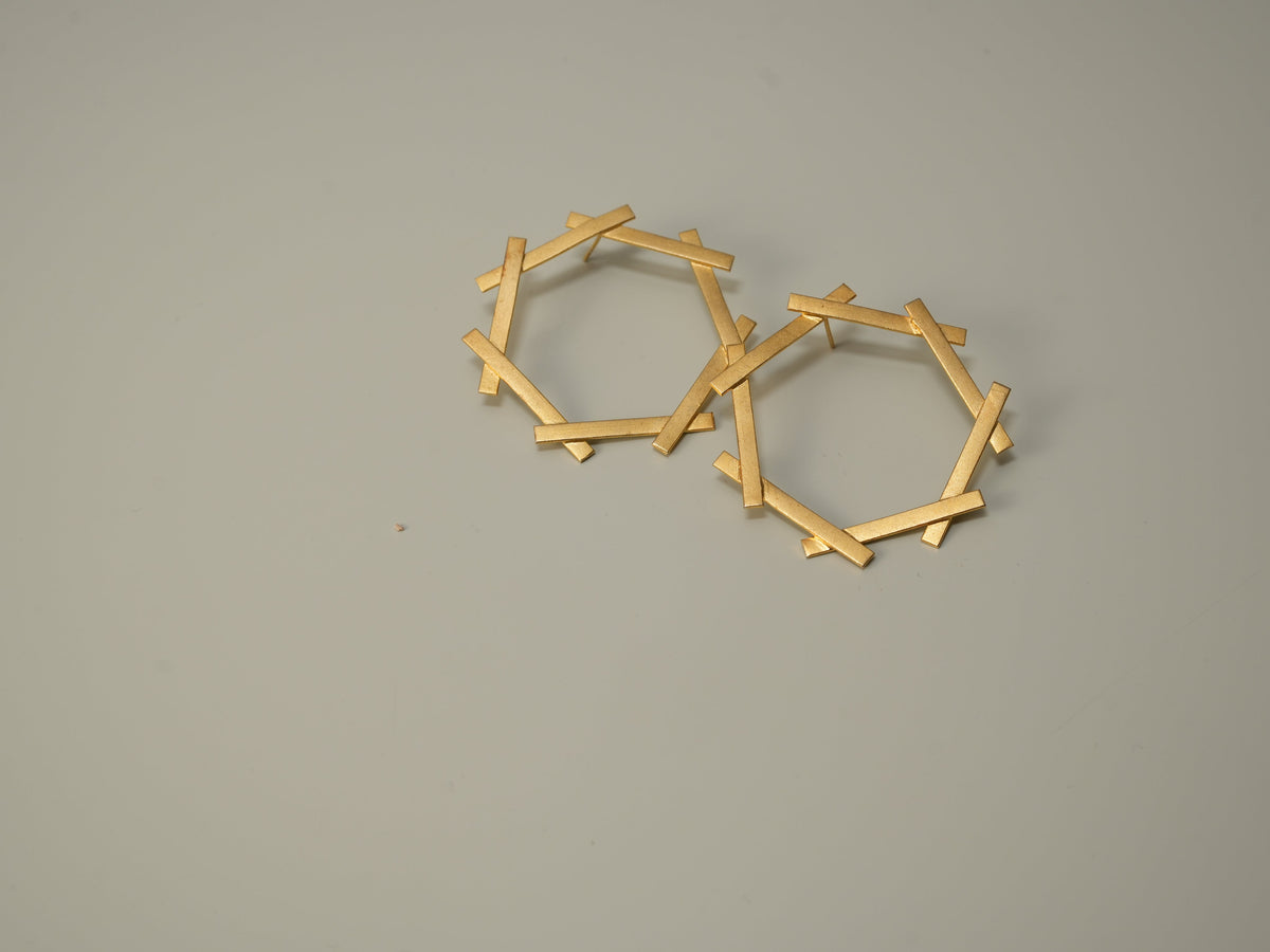 Daga-accessories gold hexagon stud earrings with a geometric stick-like frame design on a neutral background