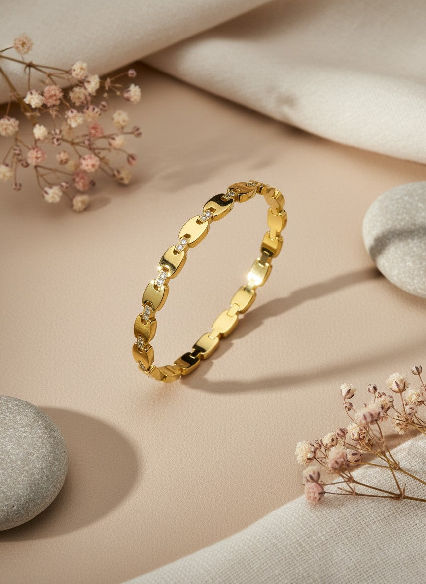 Daga-accessories gold-toned link bangle bracelet with shimmering stone accents on a neutral fabric and stone background