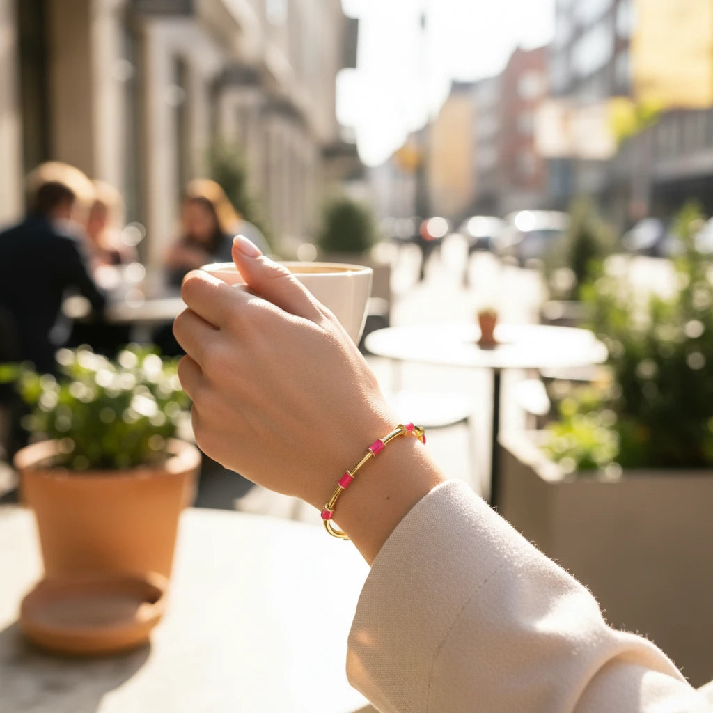 Daga-accessories minimalist gold-tone cuff bracelet with neon pink enamel dots worn on a wrist at an outdoor cafe