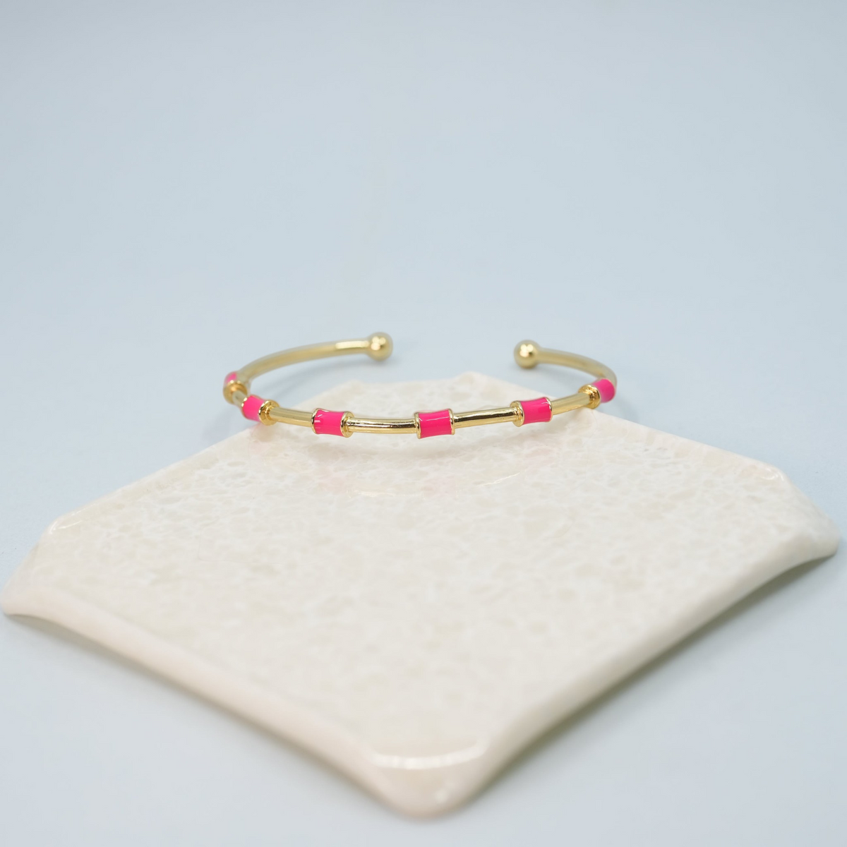 Daga-accessories minimalist gold-tone open cuff bracelet featuring vibrant neon pink enamel dot accents.