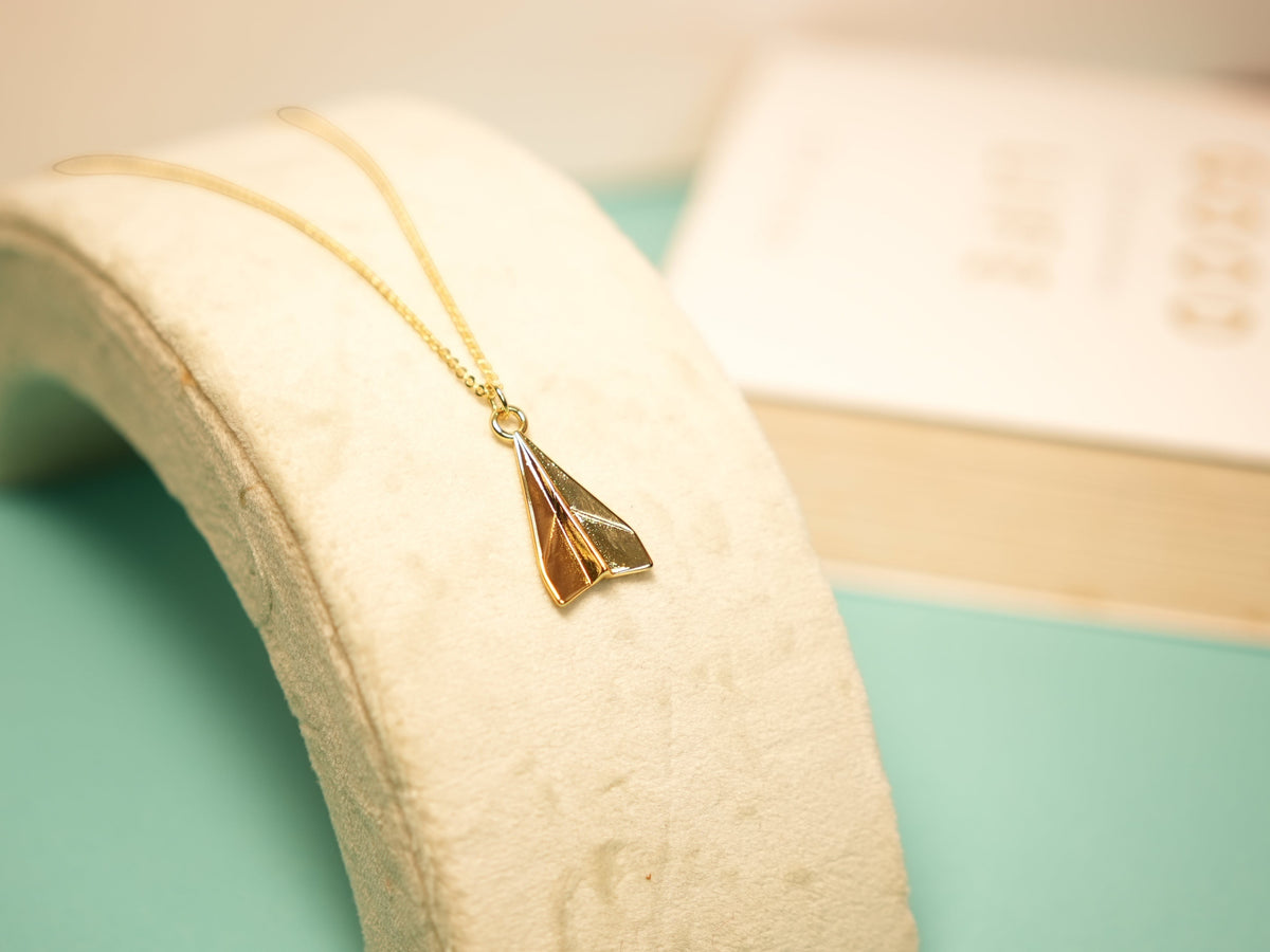 Daga-accessories dainty gold-tone paper airplane pendant necklace on a minimalist display stand