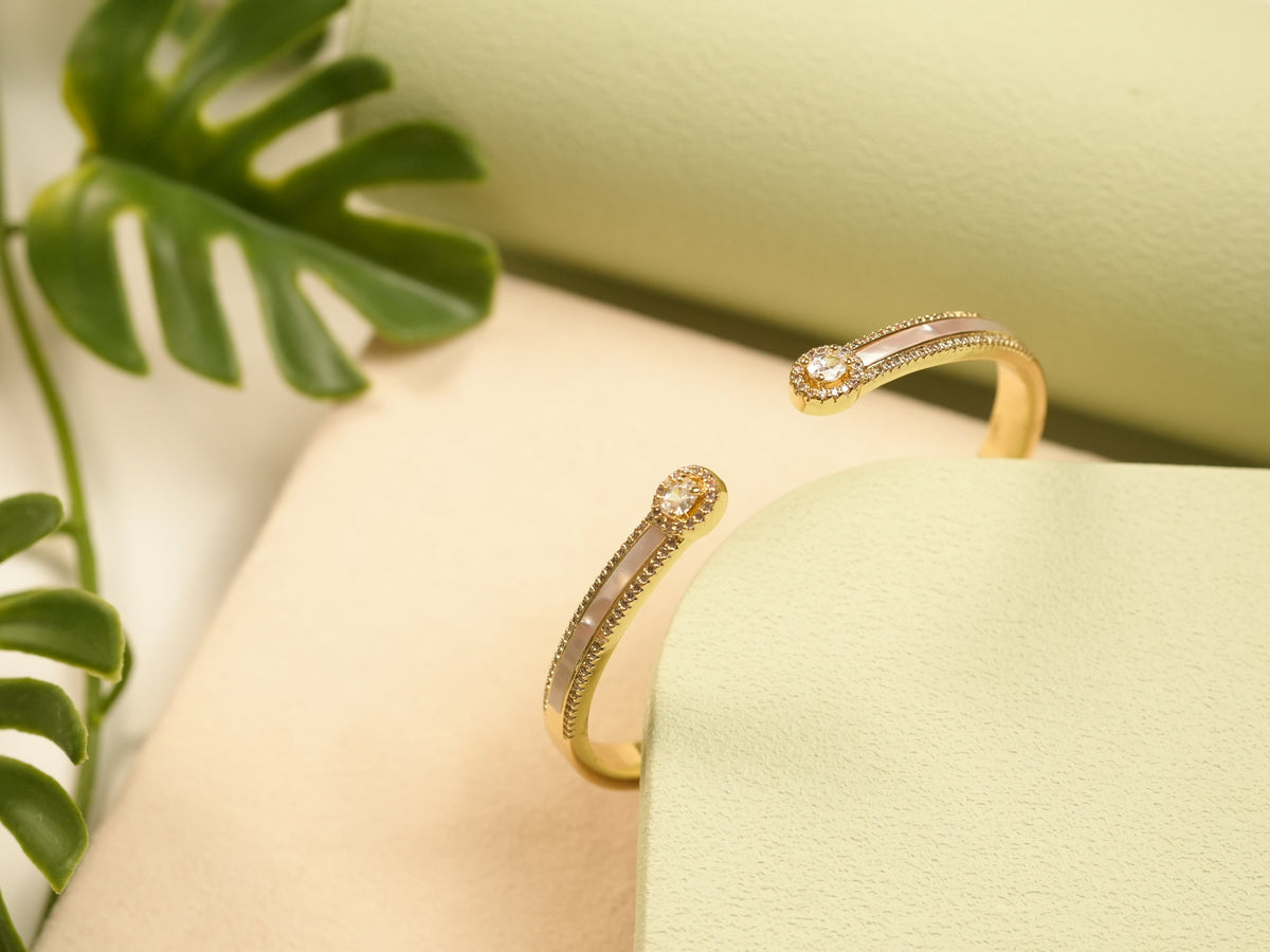 Daga-accessories gold cuff bracelet featuring lustrous pearl inlay and sparkling crystal studs on a green display.