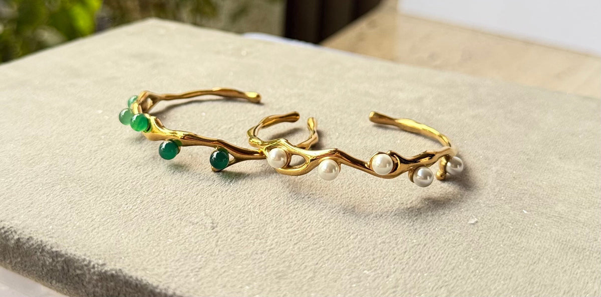Daga-accessories gold cuff bracelets featuring organic wavy bands with white pearls and green gemstone accents.