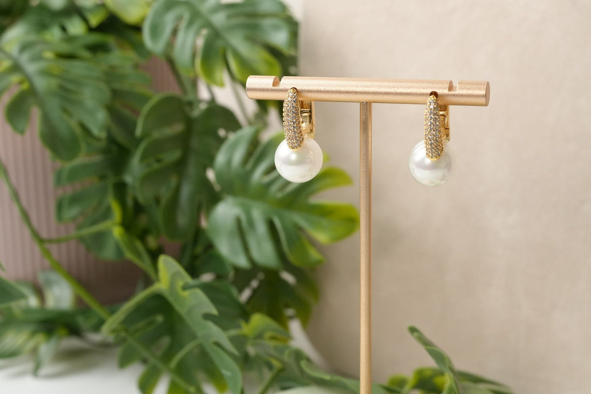 Daga-accessories gold-toned huggie hoop earrings with cubic zirconia and a lustrous faux pearl drop on a display stand.