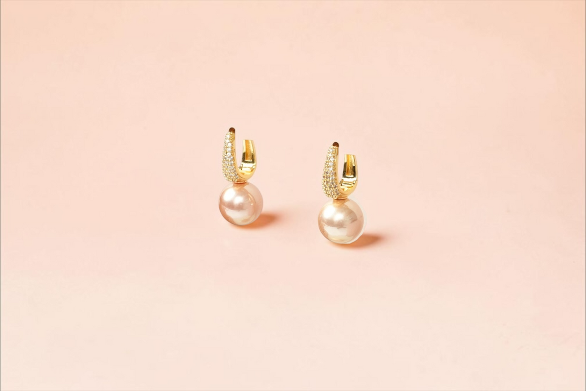 Daga-accessories gold-toned hoop earrings with cubic zirconia and soft-pink pearl drops on a display stand.